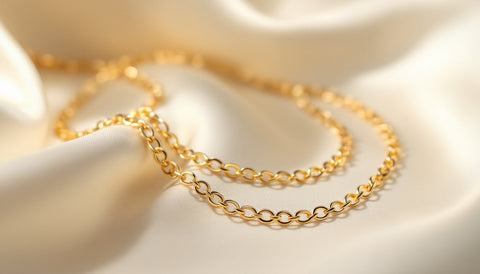 Close-up of a fine gold rolo chain necklace with small round interlocking links coiled on a cream fabric surface