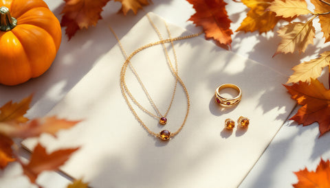 Gold-toned layered necklace, citrine earrings, and a garnet ring styled on linen with autumn leaves for a Thanksgiving jewelry gift guide