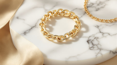 Bold gold chain bracelet with oval links next to a thin gold chain necklace on white marble, Tiffany HardWear inspired styling