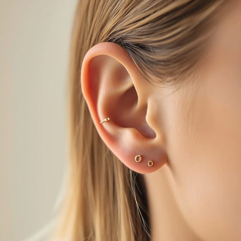 Types of ear piercings — gold studs, huggie hoops, and cartilage jewelry displayed on a woman's ear