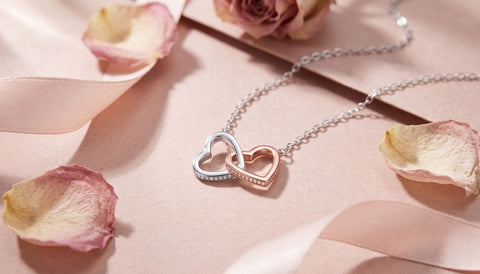 Two-tone interlocking hearts necklace on rose-colored paper with dried rose petals and ribbon