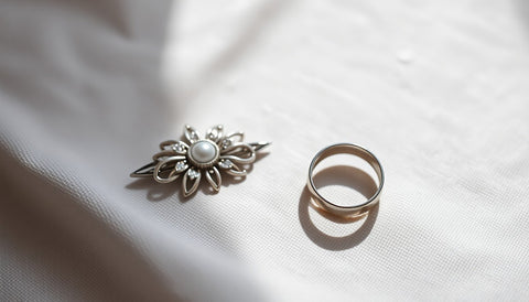 A silver tone brooch and a plain ring on a pale linen cloth