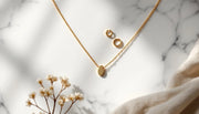 Minimalist gold necklace, small hoop earrings and dainty ring flat-lay on white marble — AJLuxe everyday jewelry