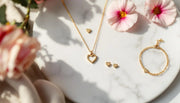 Gold heart pendant necklaces and heart stud earrings flat-lay on white marble — AJLuxe heart jewelry collection