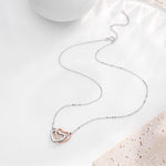Lade Bild in die Galerieansicht, Interlocking Hearts Necklace flat lay, two-tone silver and rose gold heart pendant with chain and lobster clasp, soft styled background

