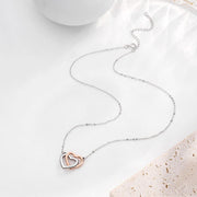 Interlocking Hearts Necklace flat lay, two-tone silver and rose gold heart pendant with chain and lobster clasp, soft styled background