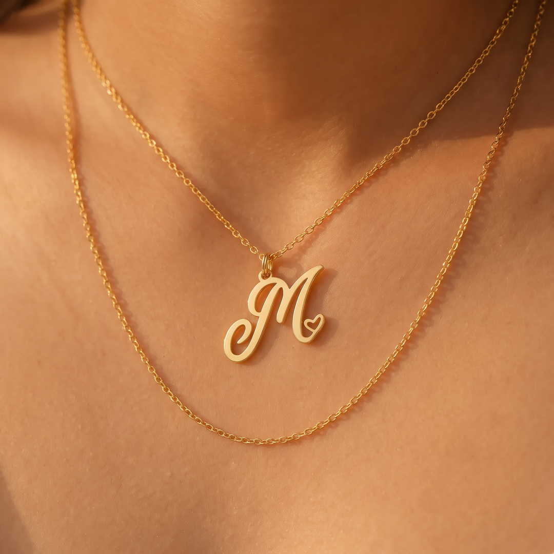 Gold heart initial necklace layered above a longer chain on a woman's neckline