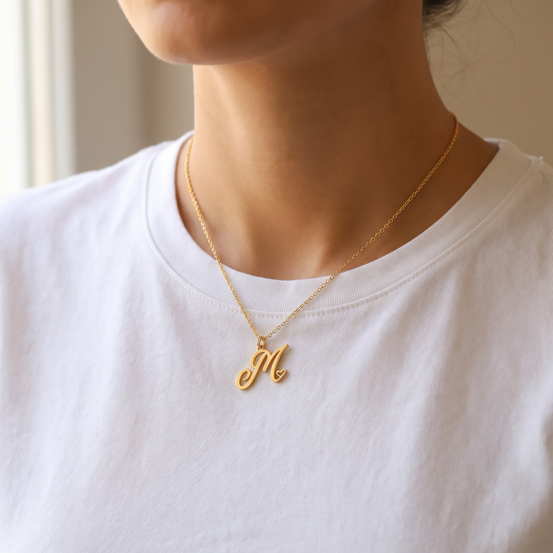 Woman wearing a gold heart initial necklace at the 18 inch setting over a white crew neck t-shirt